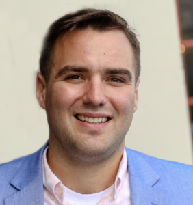 Portrait of Isaac Garrison, a professional in communications management, wearing a blue blazer over a light shirt. Isaac serves as the Communications Content Manager at Philadelphia Yearly Meeting (PYM), shaping PYM’s digital presence and storytelling efforts.